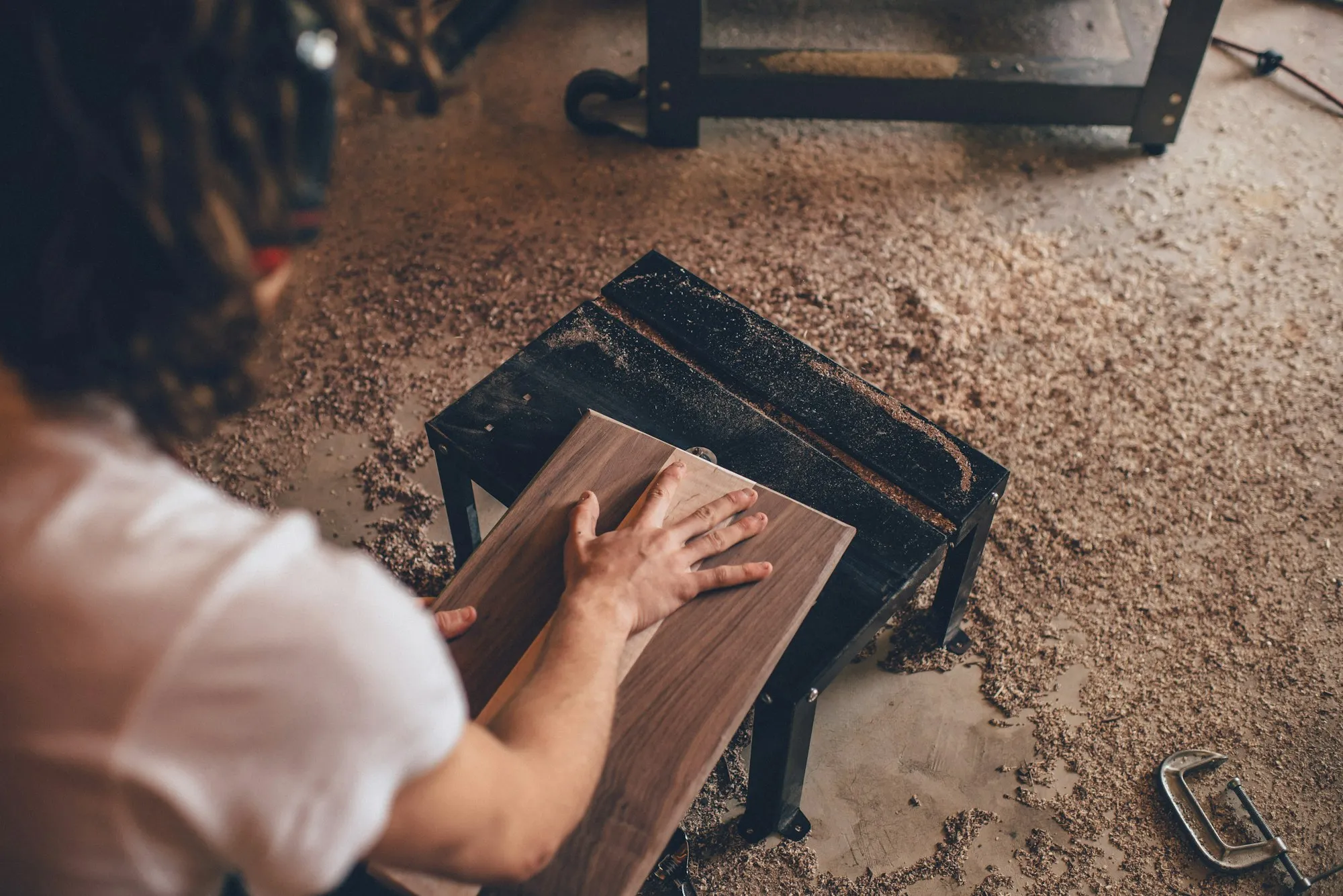 Hände führen ein Nussbaumbrett über die Maschine, Späne auf dem Werkstattboden