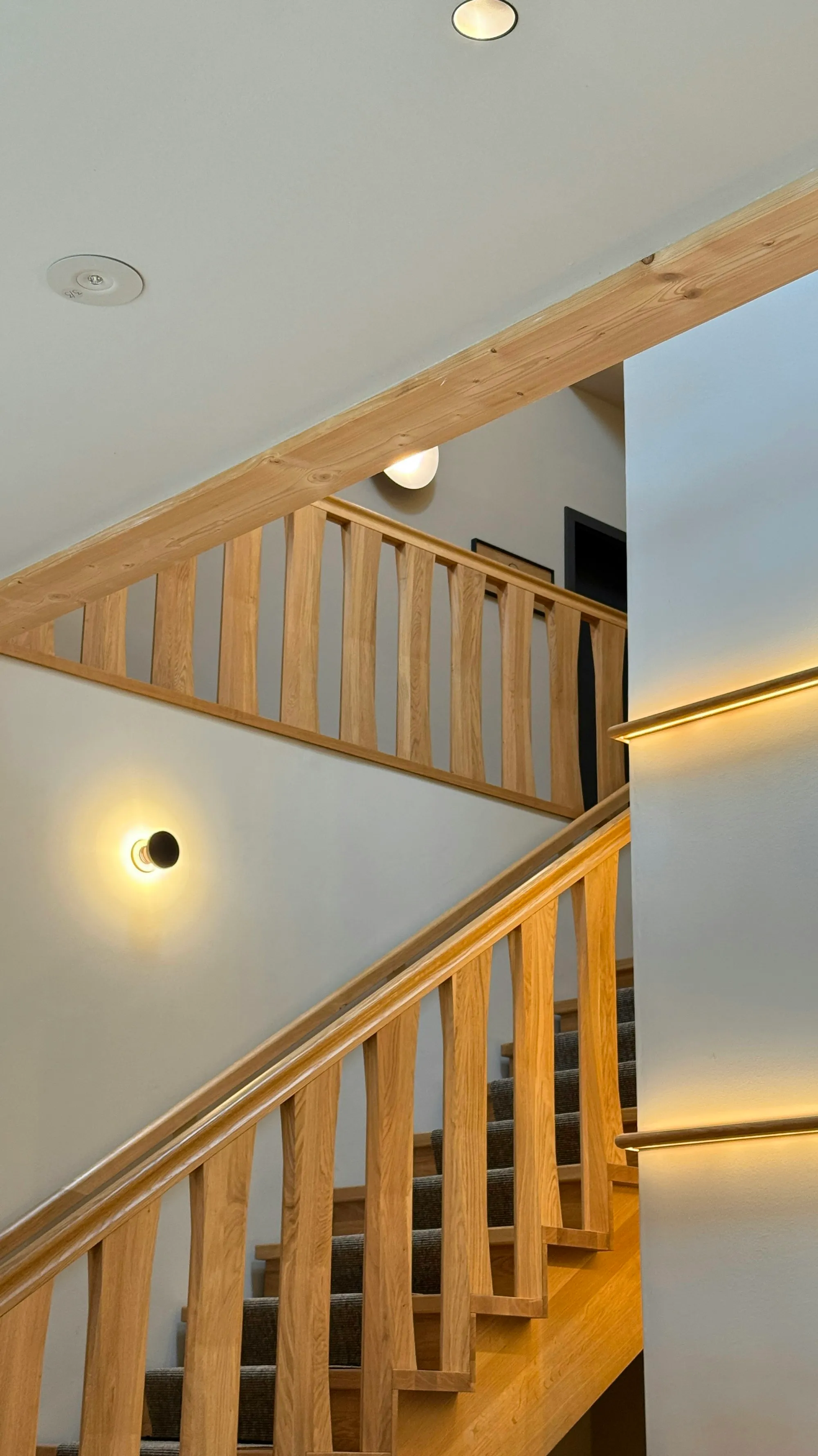 Treppe mit Eichenstufen und einem Geländer aus schmalen senkrechten Lamellen, warm ausgeleuchtet